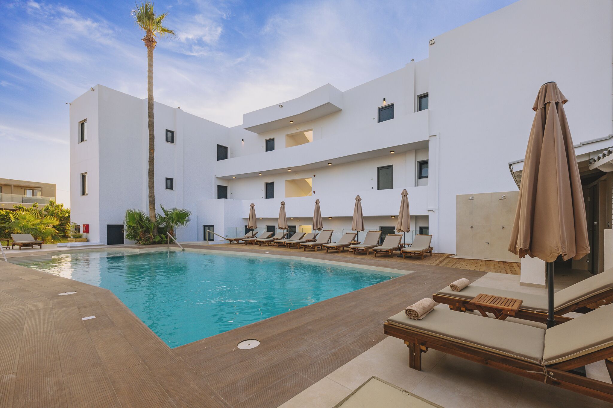 A modern hotel with a swimming pool, sun loungers, and a palm tree.