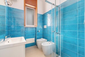 Um banheiro com azulejos azuis, pia, vaso sanitário e bidê.