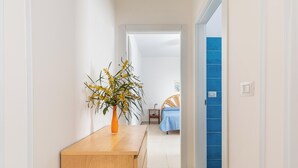A hallway with a wooden bench and a vase of yellow flowers. A bed with a blue bedspread is visible in the background. - 3873 Residence Kalura - Bilo 5 by Barbarhouse (Porto Cesareo)