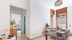 A dining area with a table set for four, a white chair, and a small side table with a television. - 3873 Residence Kalura - Bilo 5 by Barbarhouse (Porto Cesareo)