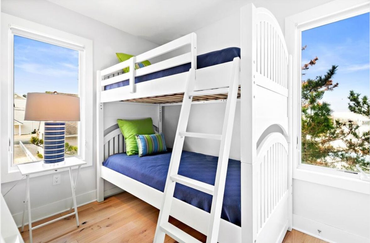 Een stapelbed met een ladder, een raam met uitzicht op bomen, en een lamp op een klein tafeltje.