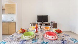 Een eetgedeelte met een tafel voor vier personen, een televisie en een keuken op de achtergrond.
