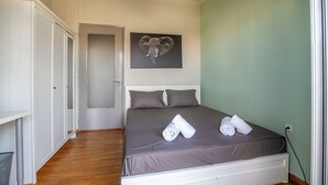 Een slaapkamer met een bed, kussens, een aan de muur hangend kunstwerk van een olifant, en een deur naar een andere kamer.