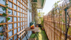 A wooden table with a bowl of fruit and a potted plant, set against a bamboo fence and a wall with climbing plants. - Acropolis Rooftop View! 10 Minutes From Everywhere (Athina)