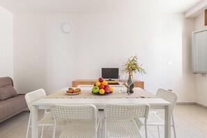 A dining area with a table set for four, a television in the background, and a sofa to the left. - 3875 Residence Kalura - Trilo 2 by Barbarhouse (Porto Cesareo)