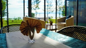 A room with a table, chairs, a vase with a decorative item, and a view of the outdoors. - Eben Lake Kivu Cottages and Villas (Kagano)