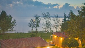 A building with a red-tiled roof, a well-lit entrance, and a view of a body of water. - Eben Lake Kivu Cottages and Villas (Kagano)