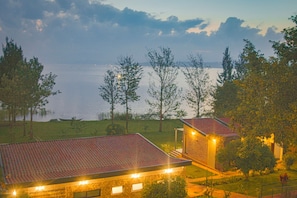 A building with a red-tiled roof, a well-lit entrance, and a view of a body of water. - Eben Lake Kivu Cottages and Villas (Kagano)