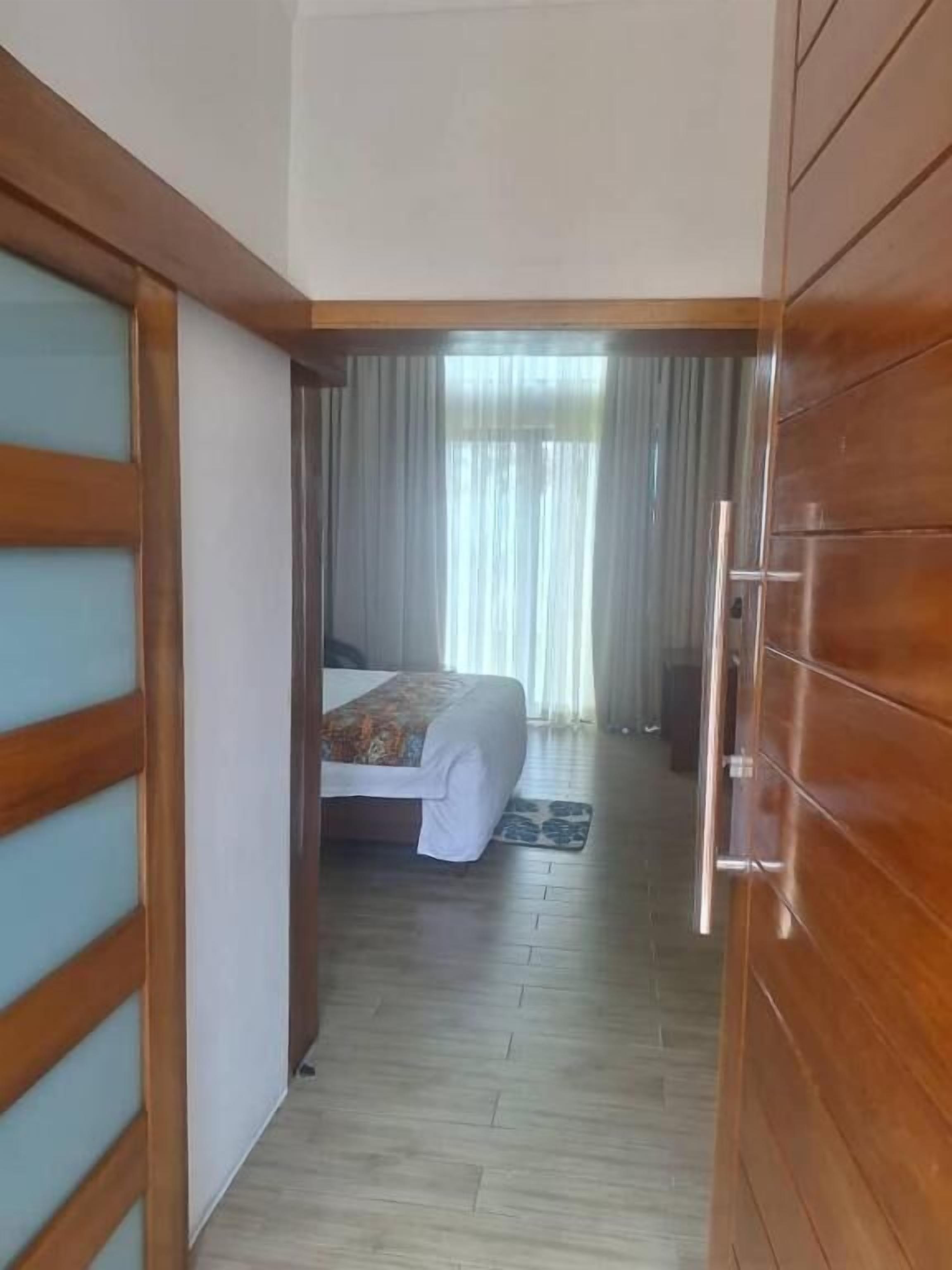 A hotel room with a wooden wardrobe, a bed with a patterned bedspread, and a view through a window with curtains.