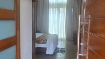 A hotel room with a wooden wardrobe, a bed with a patterned bedspread, and a view through a window with curtains.