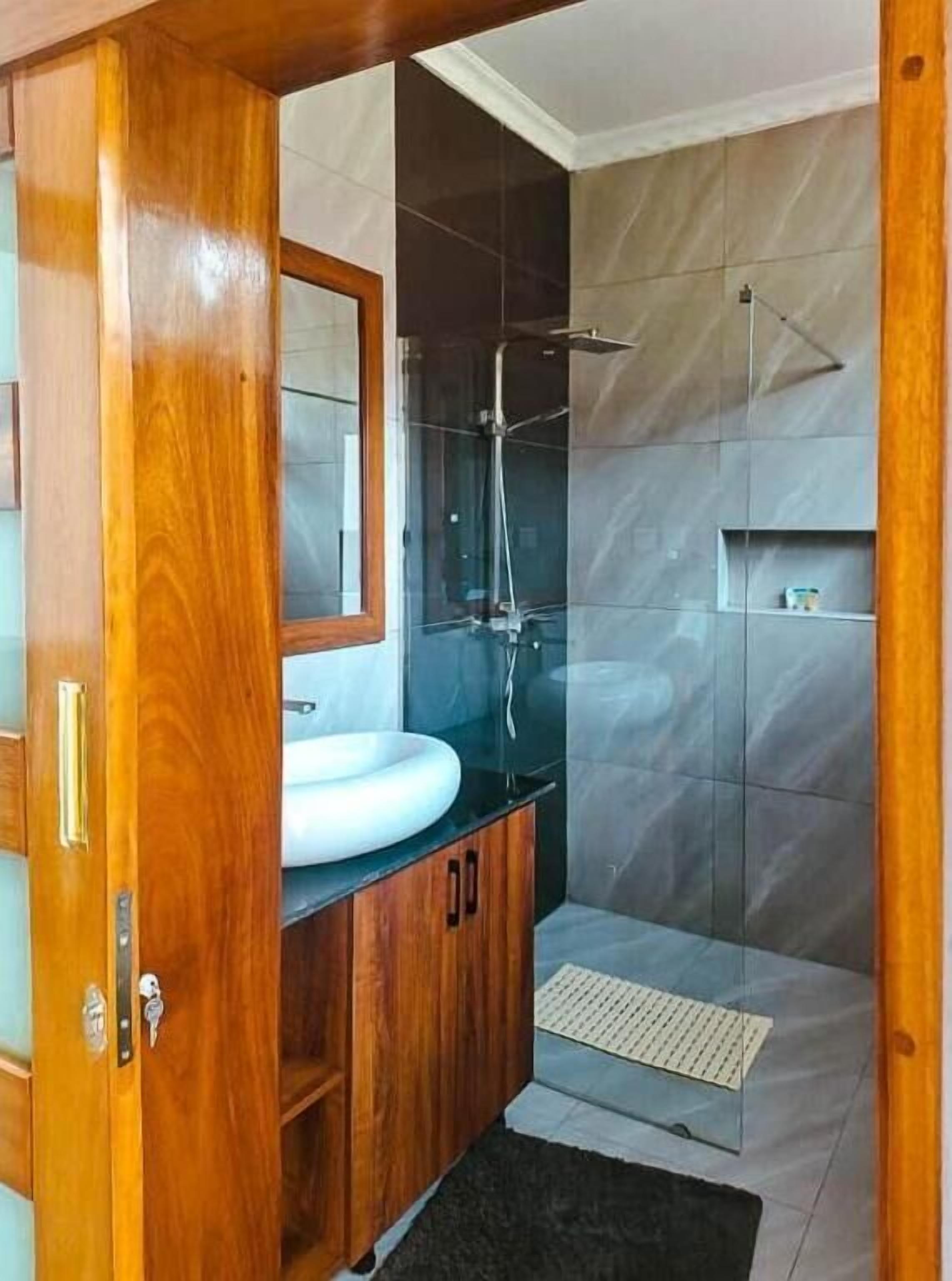 A modern bathroom with a wooden vanity, a large mirror, a glass shower enclosure, and grey tiled walls.