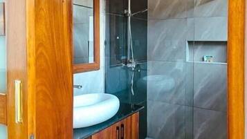 A modern bathroom with a wooden vanity, a large mirror, a glass shower enclosure, and grey tiled walls.