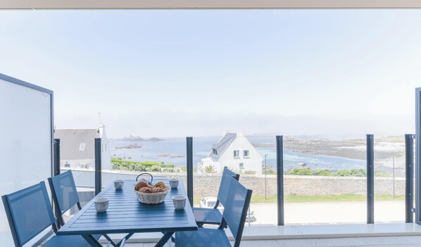 A balcony with a table set for breakfast, overlooking a coastal landscape with buildings and a view of the sea. - Ty Moutik - Lovely luxury T2 flat with sea view (Porspoder)