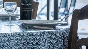 A table with a bottle of Mouton Cadet Bordeaux, two glasses, and a plate, set against a backdrop of a large window overlooking a marina.