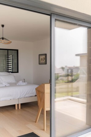 A modern bedroom with a bed, a wooden chair, a framed picture, and a view through a sliding glass door. - Ar Skol - Magnificent seafront duplex (Porspoder)
