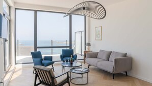 Una sala de estar moderna con un ventanal grande, un sofá gris, sillones azules y una mesa de centro redonda.