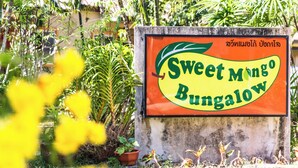 Señal para Sweet Mango Bungalow, con un jardín tropical de fondo.