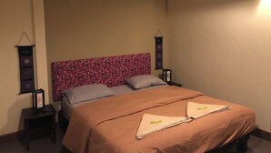 Una cama bien hecha con cabecera de flores, una mesita de noche con lámpara y un equipo de aire acondicionado en la pared.