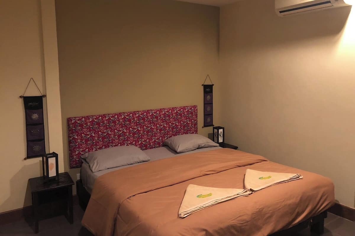A neatly made bed with a floral headboard, a bedside table with a lamp, and an air conditioning unit on the wall.