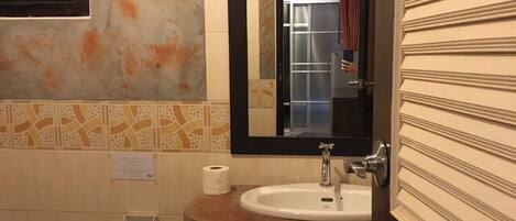Un baño con lavamanos, espejo, inodoro y cubo de basura.