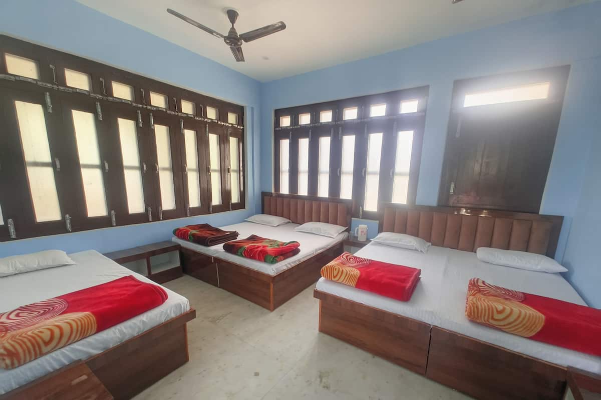 A hotel room with three wooden beds, each with a red and orange patterned blanket. There are large windows with multiple panes, and a ceiling fan is visible.