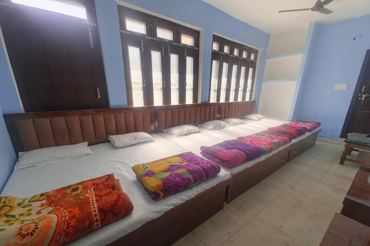 A room with a long bed, two windows with blinds, a ceiling fan, and a door.