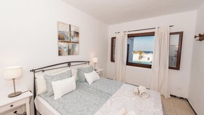 A neatly arranged bedroom with a bed, bedside tables, and a window with curtains. - Fkk-apartment in Villa Blanca, 4 mit Schwimmbad und Zwei Schlafzimmer (Charco del Palo)