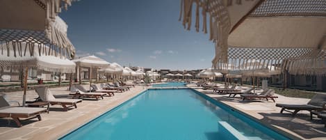 Zona de piscina con sillas de descanso y sombrillas, rodeada por un cielo despejado.