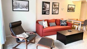 Un salon avec un canapé rouge, deux fauteuils, une table basse et trois tableaux encadrés accrochés au mur.