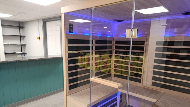 Un espace de bureau moderne doté d’une cloison en verre, d’un comptoir avec un évier et d’un plafond pourvu d’un éclairage encastré.