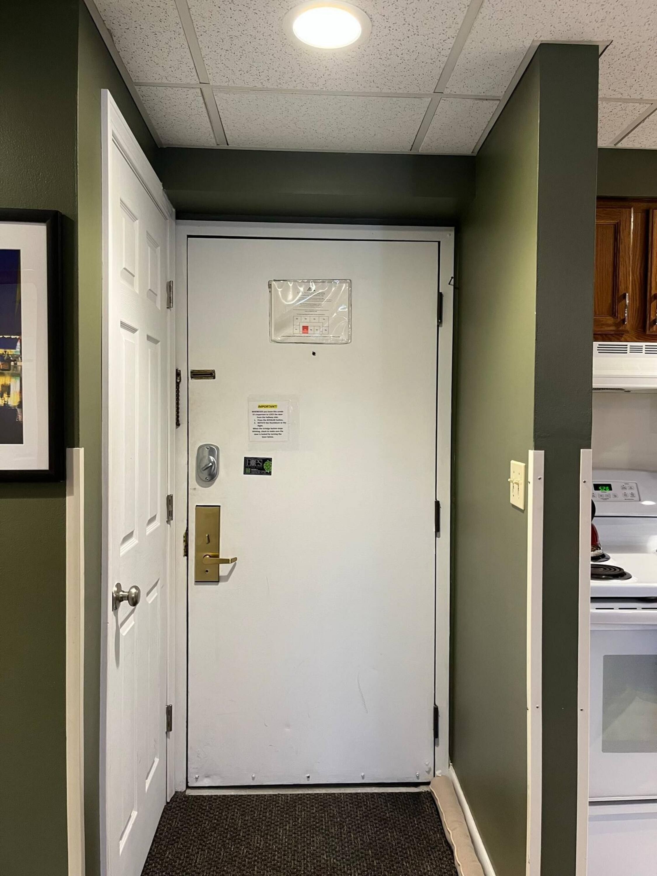 A hallway with a white door, a thermostat, and a small sign on the wall.