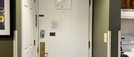 A hallway with a white door, a thermostat, and a small sign on the wall.