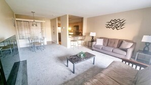 A spacious living room with a grey sofa, a coffee table, and a dining area with chairs and a table. - Amazing 2 Bedroom 2 Bath Condo (Elkins Park)