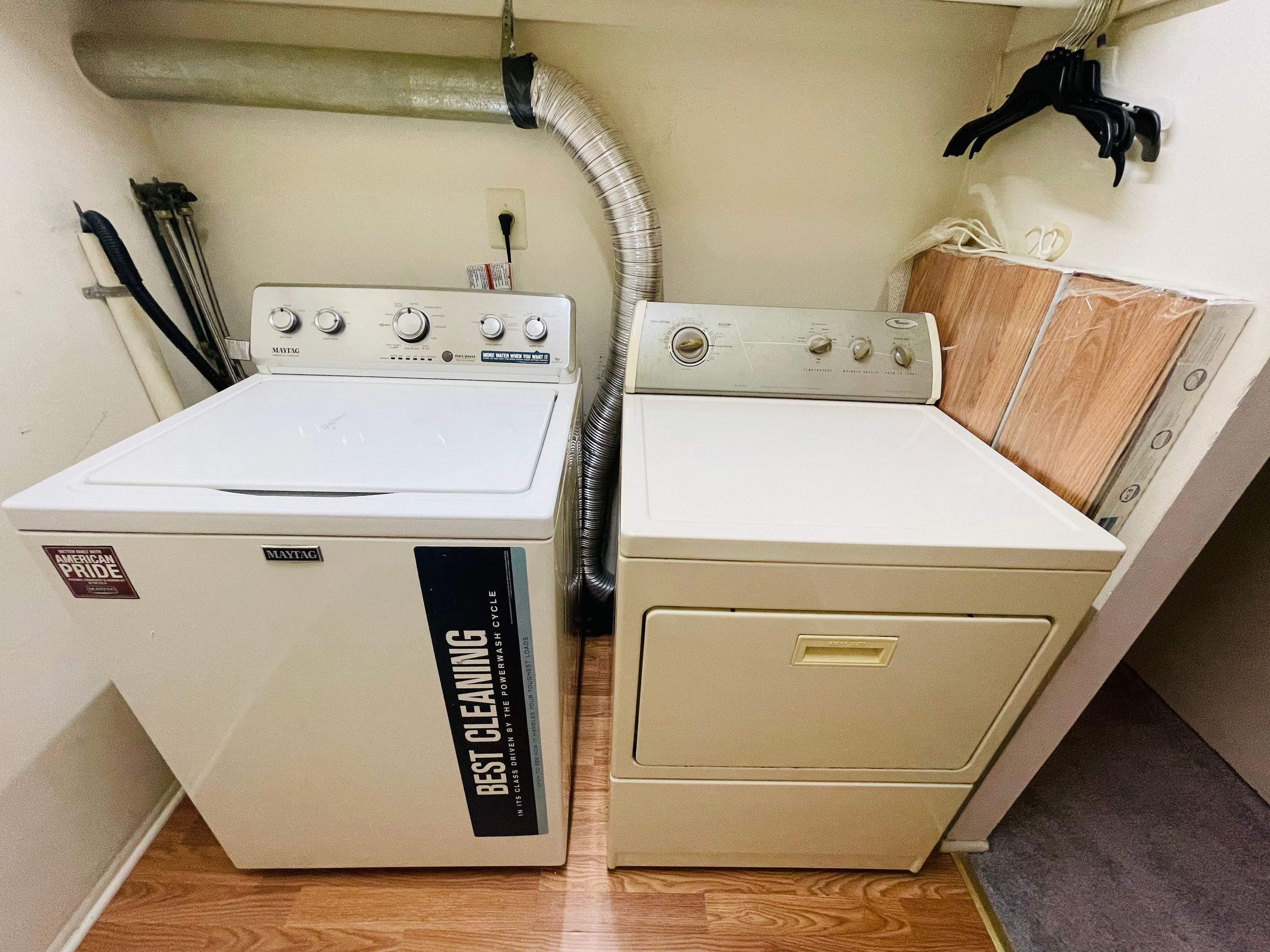 A laundry room with two Maytag washers and dryers, a vent hose, and a wooden cabinet.