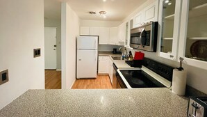 A modern kitchen with white cabinets, a stainless steel microwave, and a red cutting board. - Amazing 2 Bedroom 2 Bath Condo (Elkins Park)