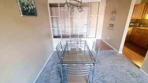 A dining area with a glass table and metal chairs, a ceiling light fixture, and a kitchen visible through an open door. - Amazing 2 Bedroom 2 Bath Condo (Elkins Park)