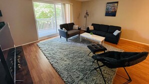 A living room with a sofa, armchair, coffee table, and a balcony with a view of greenery. - Amazing 2 Bedroom 2 Bath Condo (Elkins Park)