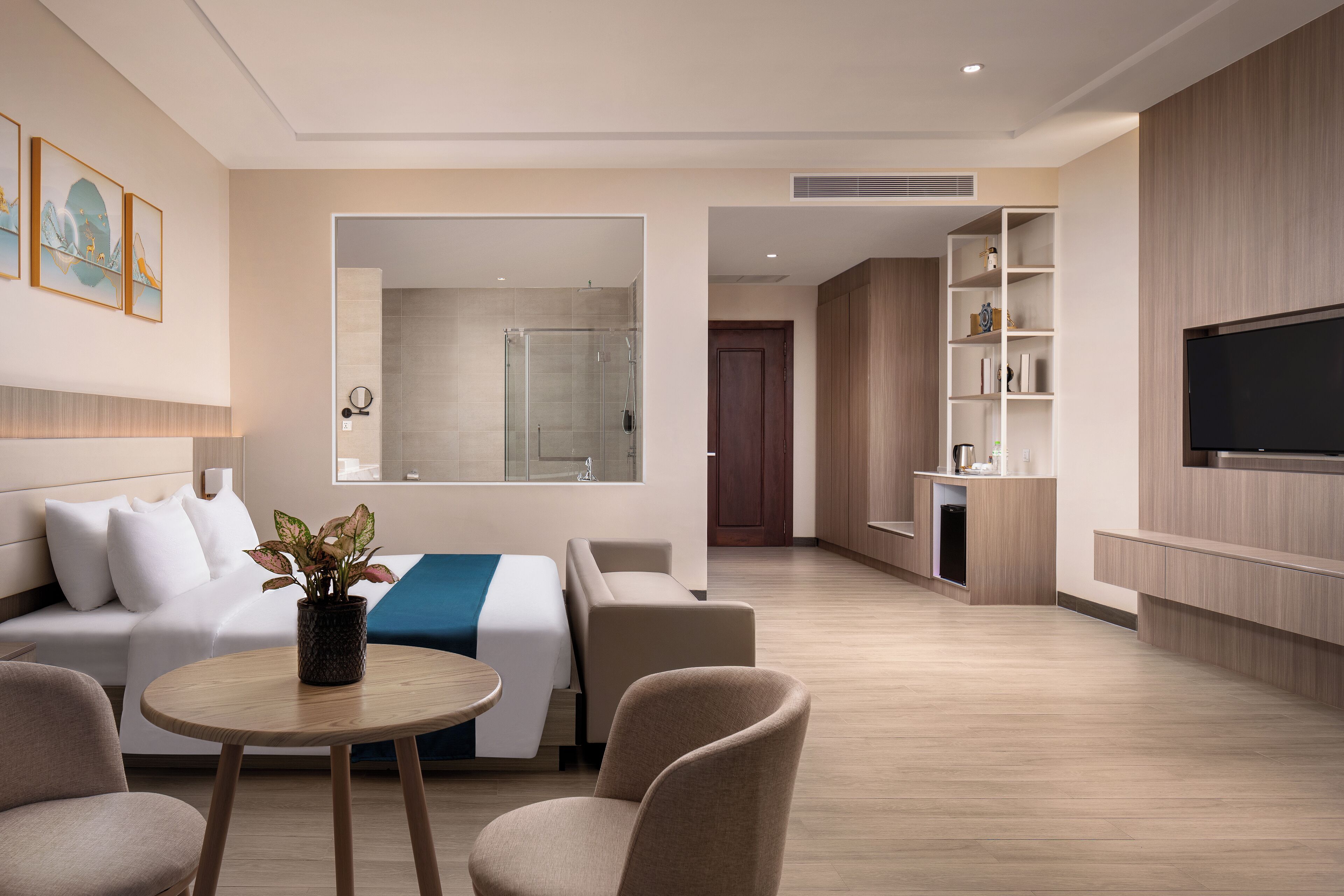 Una habitación de hotel moderna con cama, zona de estar, televisor y un baño visible a través de una puerta abierta.