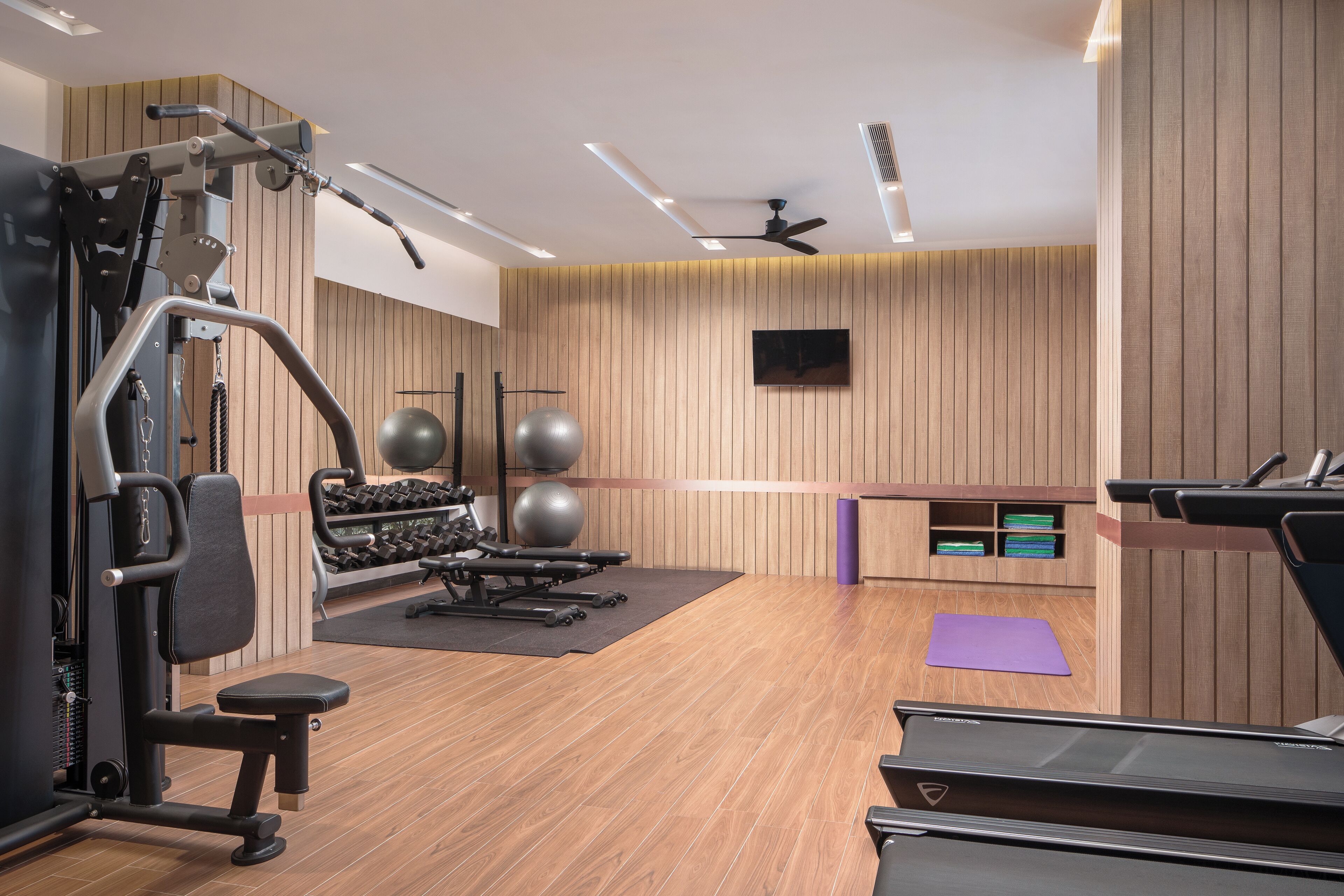 A gym with exercise equipment, a treadmill, and a wall-mounted TV.