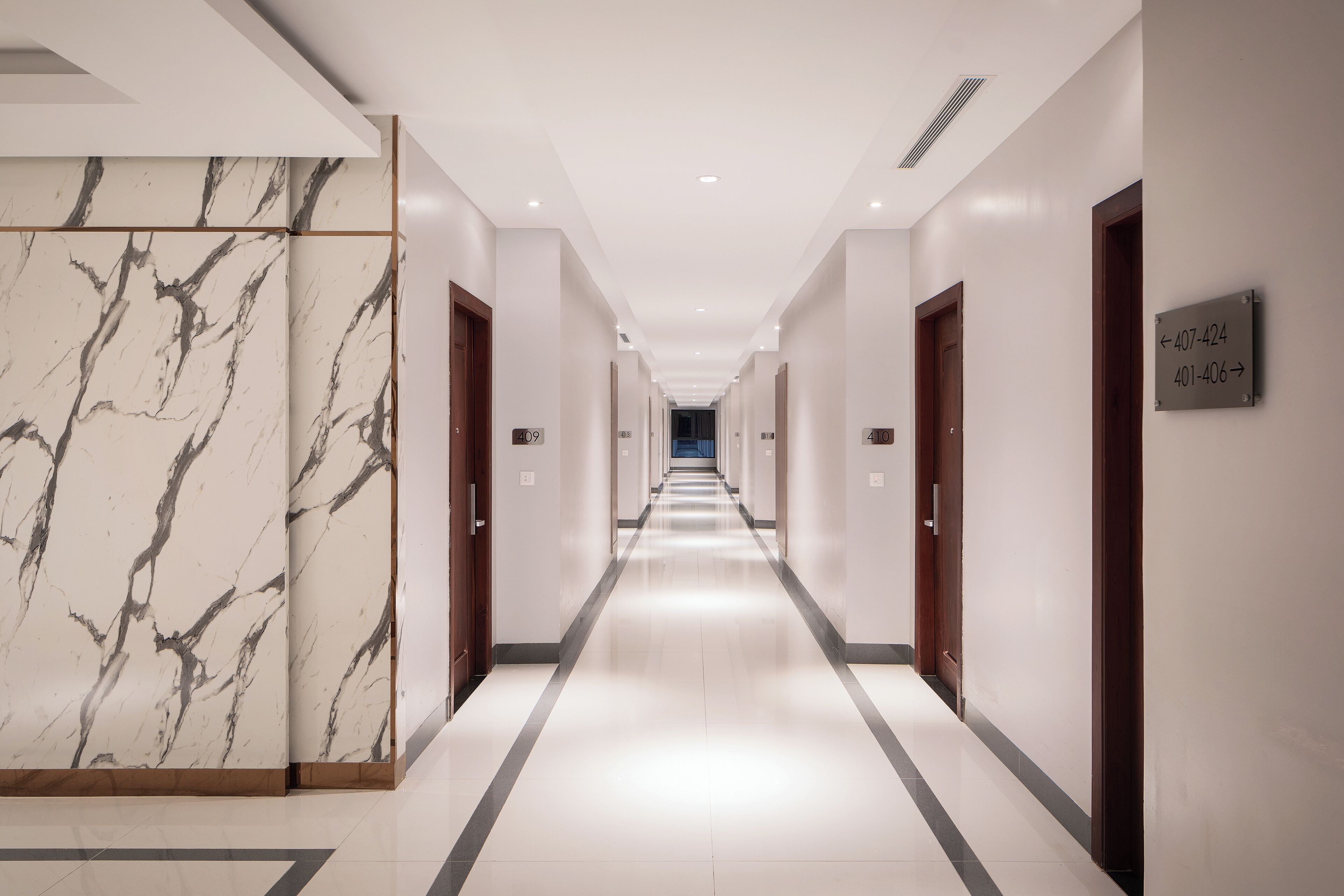 A long, well-lit hallway with marble walls and numbered doors, leading to a blue door at the end.
