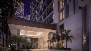 Een moderne hotelentree met een overdekte doorgang, palmbomen en een goed verlichte gevel.