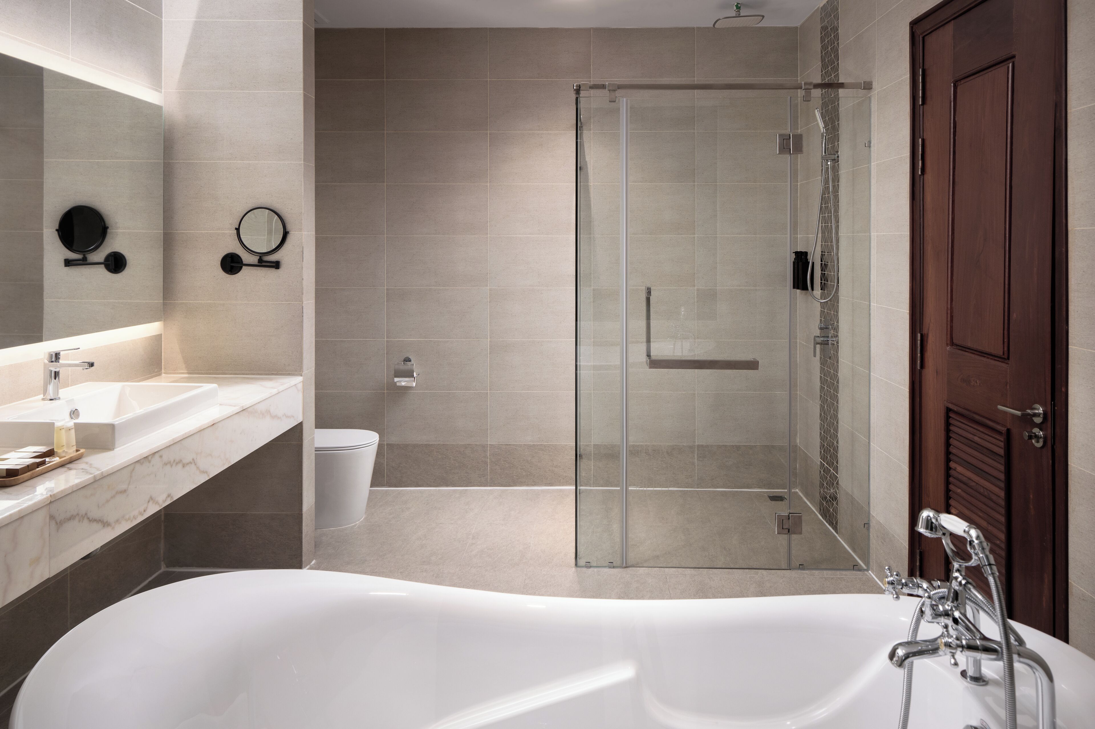Un baño moderno con una bañera grande, ducha con cerramiento de vidrio y puerta de madera.