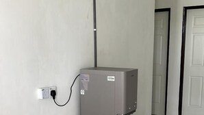 A water dispenser mounted on a wall in a hallway with tiled flooring and white doors. - SKYN SMART HOME (Ipoh)