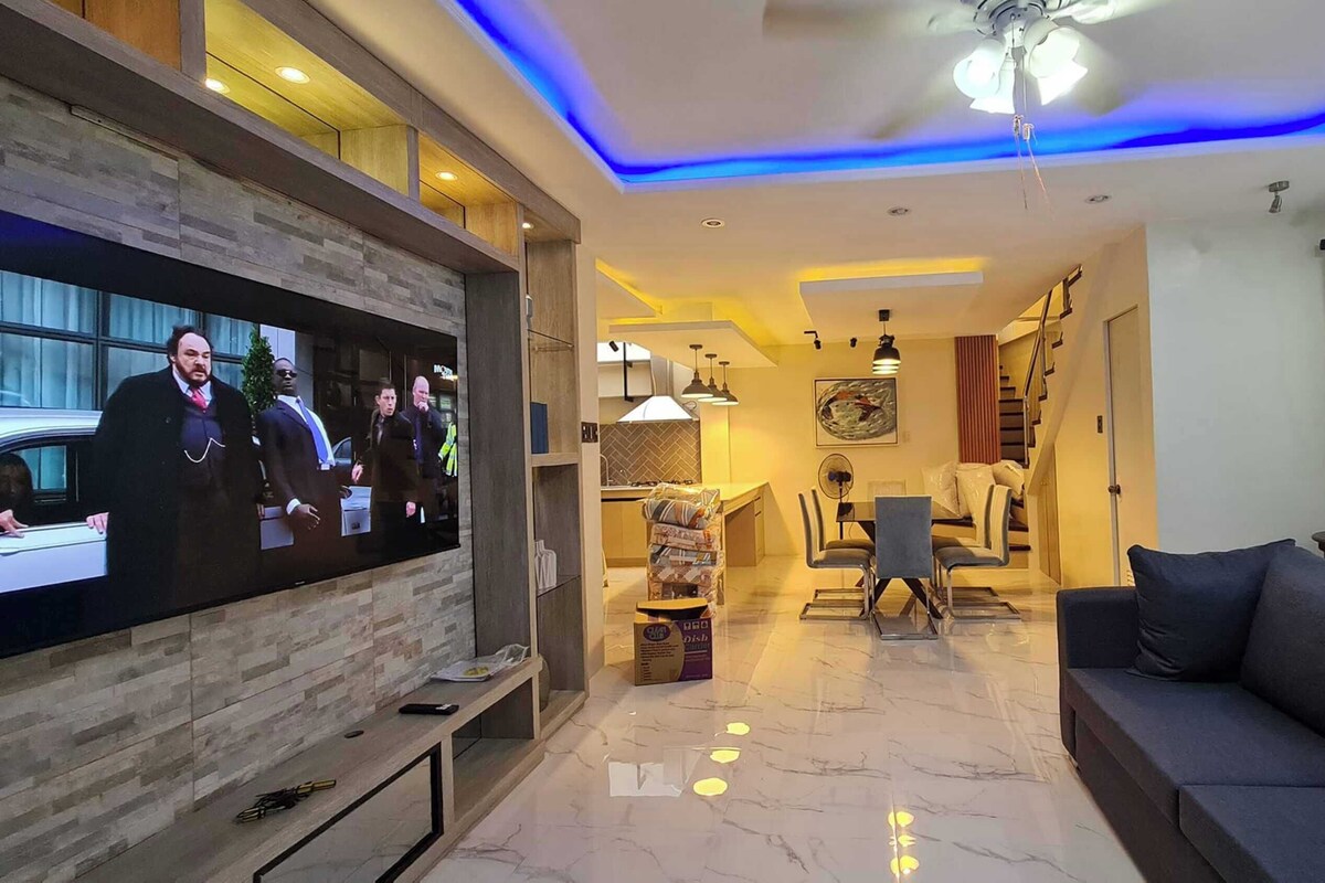 Una sala de estar moderna con una televisión de pantalla plana, un sofá, una zona de comedor y una escalera.