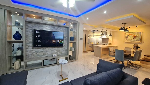 Una sala de estar moderna con un televisor de pantalla plana, un sofá y un comedor con sillas y una mesa.