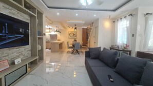 Una sala de estar moderna con un televisor de pantalla plana grande, un sofá gris y un comedor con una cocina al fondo.