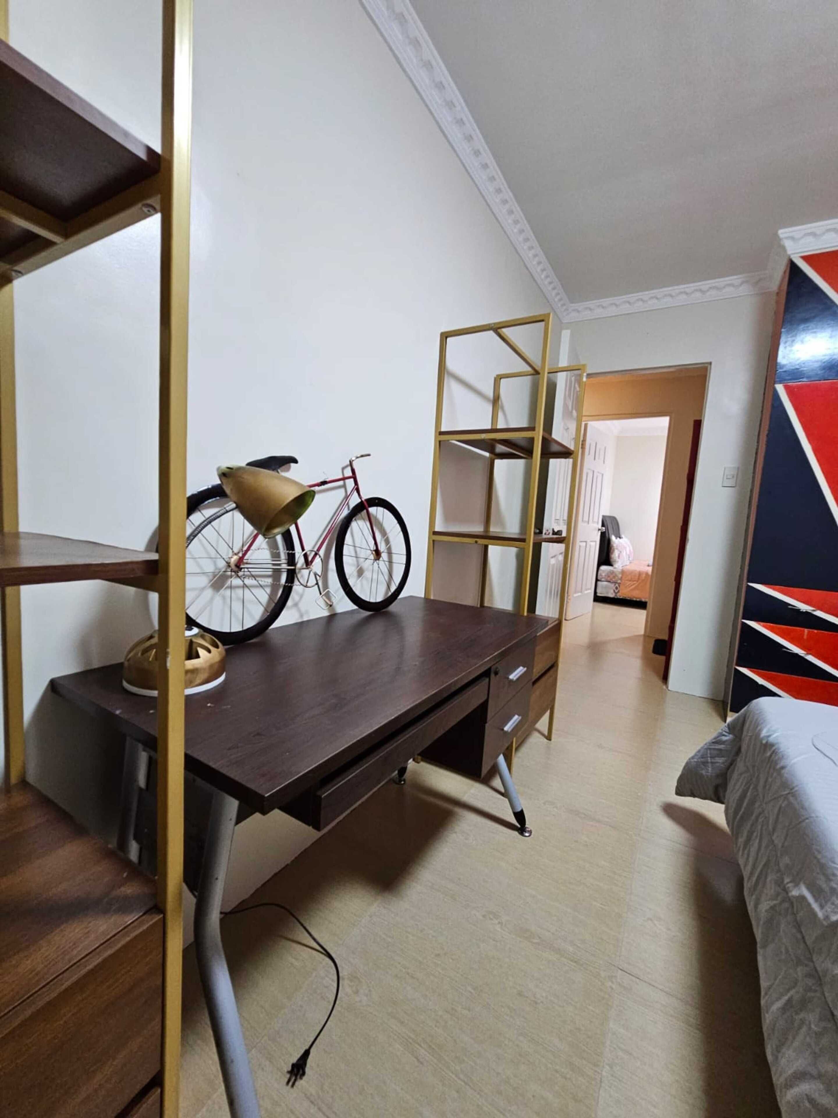 Una camera da letto compatta con una scrivania in legno, una bicicletta, una scaffalatura metallica e un letto.
