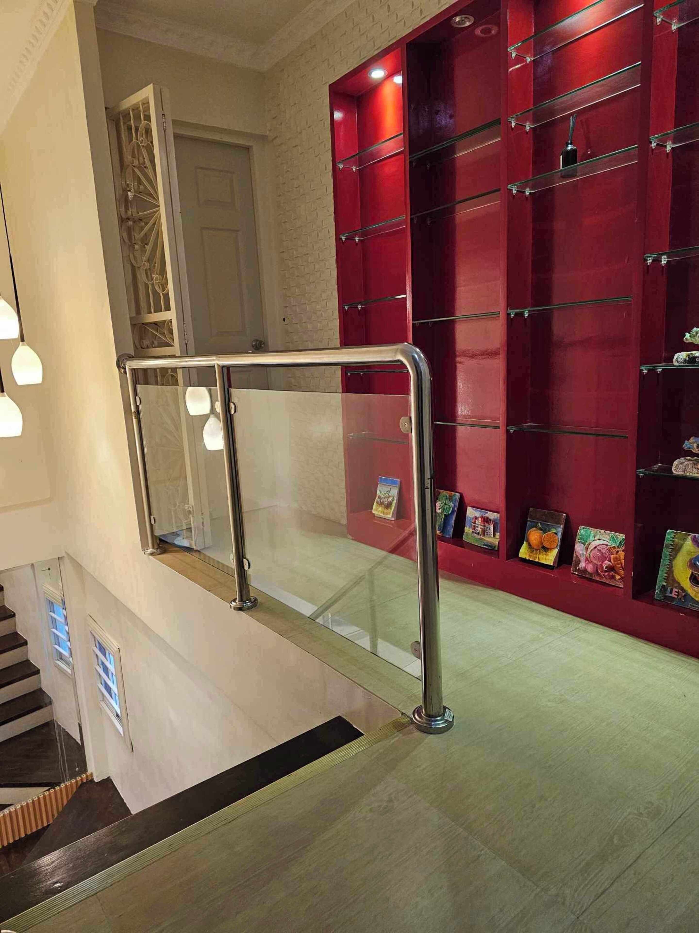 Una escalera con barandilla de vidrio y pared roja con estantes mostrando diversos objetos.