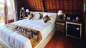 Una camera da letto con soffitto in legno, un letto con biancheria da letto bianca e cuscini decorati, un comodino con una lampada e una piccola credenza.