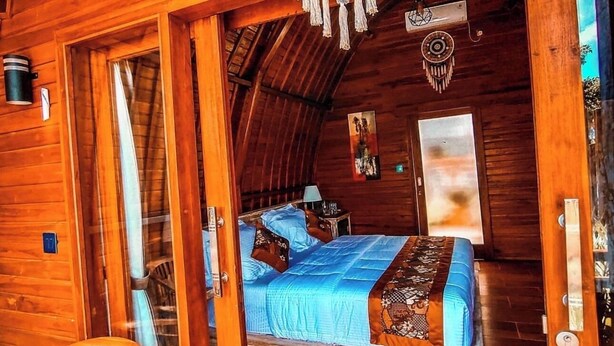 Una camera in una baita di legno, con un letto, un portafortuna e un tavolino con una lampada.